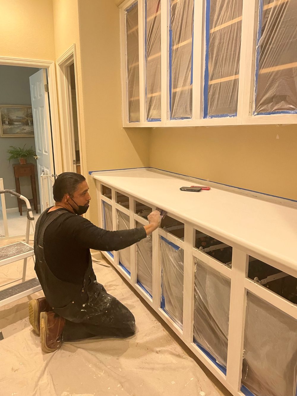 Contractor painting and refinishing kitchen cabinets with protective covering.
