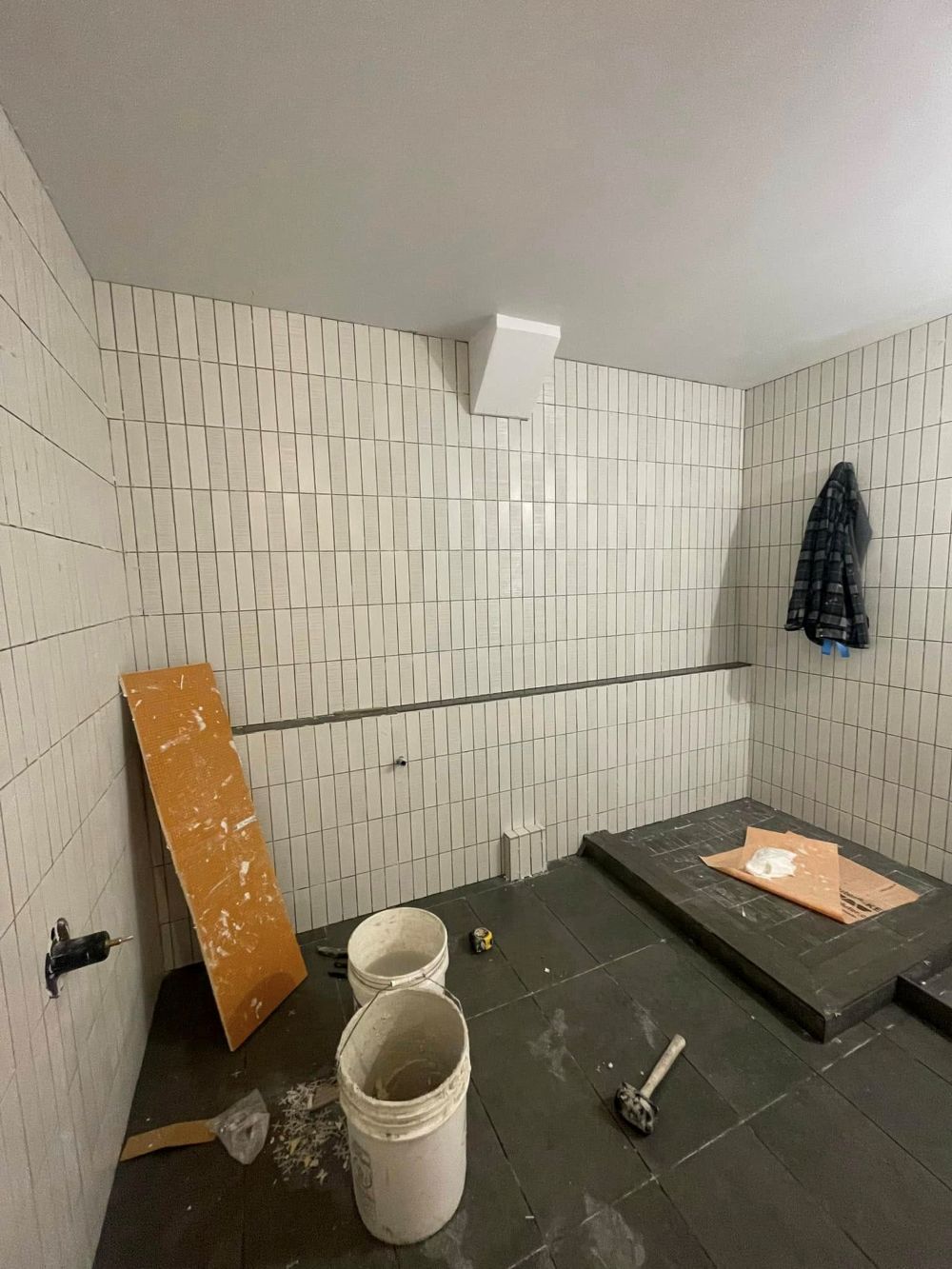 Bathroom tile installation in progress with vertically stacked wall tile and dark floor tile during a remodel.