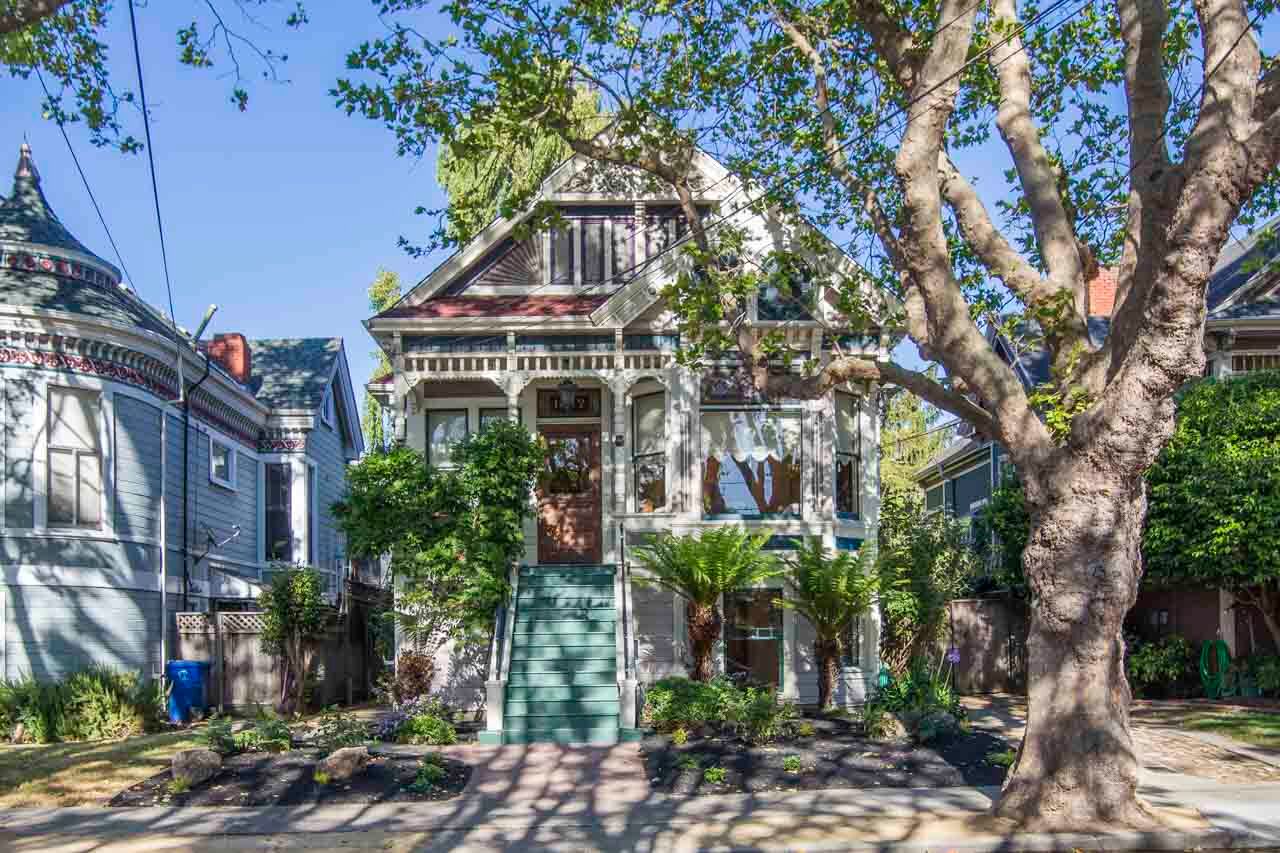 Victorian-style home with decorative trim, front stairs, and landscaped yard in a tree-lined neighborhood