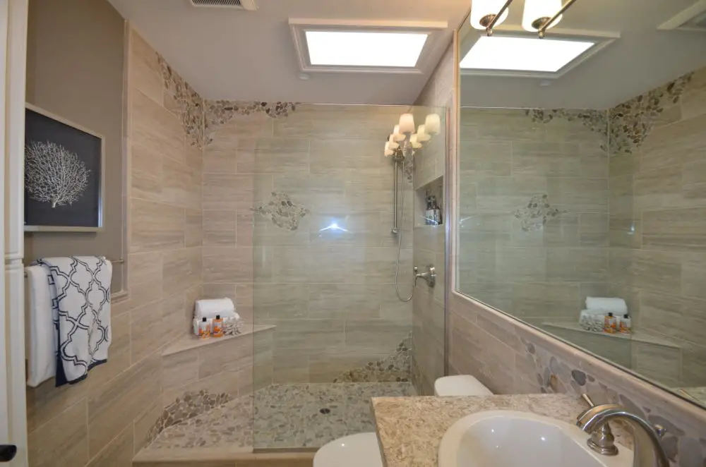 Luxury bathroom remodel featuring a frameless glass walk-in shower with decorative tile accents, granite vanity, and skylights.