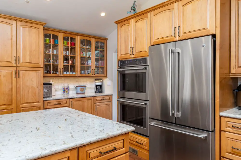 Kitchen with maple cabinets, glass upper cabinets, double oven, and stainless steel refrigerator