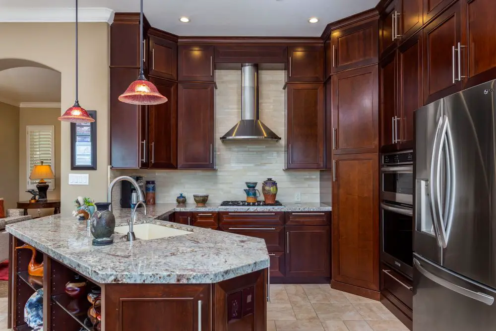 Elegant kitchen with dark wood cabinets, stainless steel appliances, island sink, and pendant lighting.