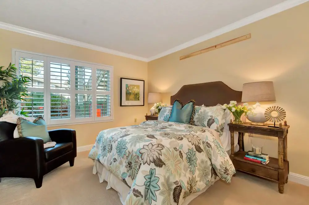 Bedroom with creamy yellow painted walls, floral bedding, wood furniture, and warm golden undertones.