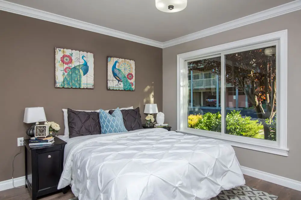 Bedroom with warm taupe painted walls, white bedding, dark nightstand, and natural light showing warm undertones.