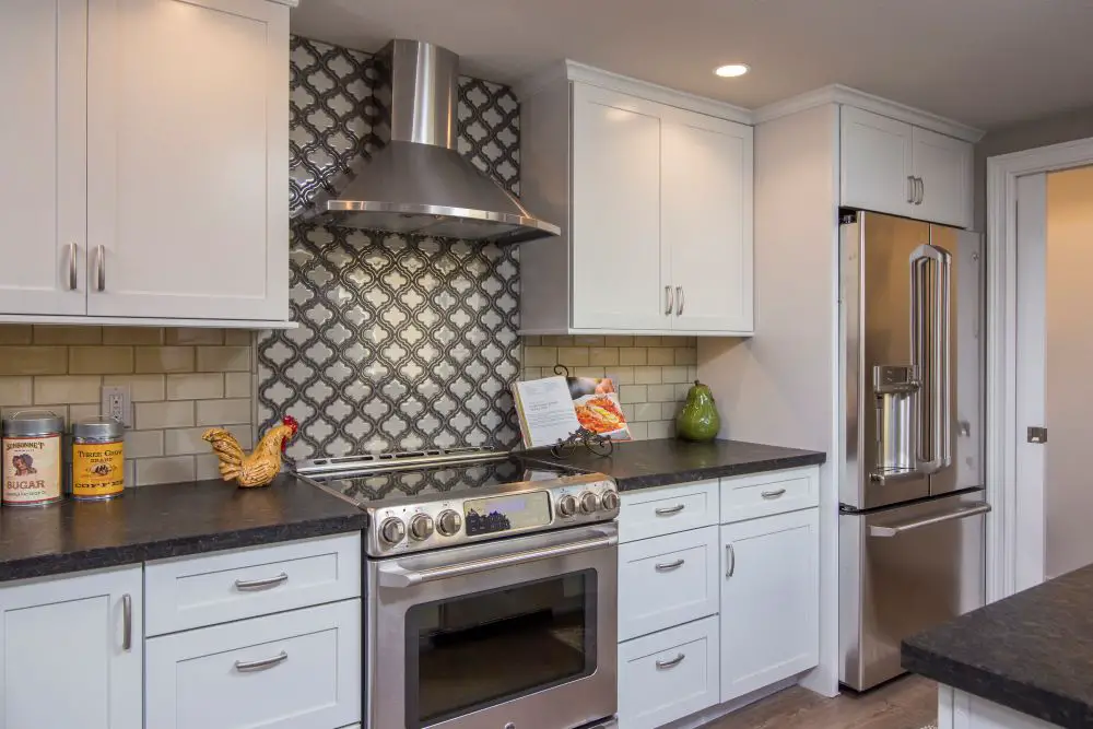 White kitchen cabinets with subway tile backsplash and decorative patterned tile behind stove.