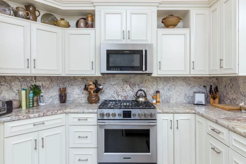 Kitchen with white cabinets and full-height granite backsplash matching countertops.