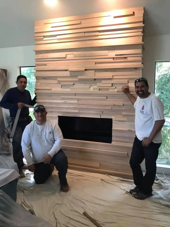 Contractors installing modern wood slat accent wall around fireplace.