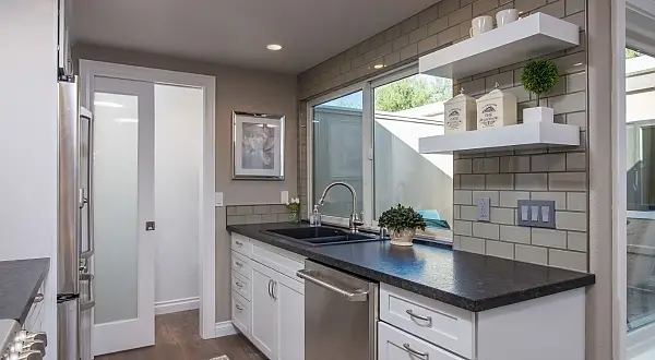 Touches of drama add interest in this complete home makeover.  In the kitchen a dramatic, patterned glass tile draws the eye as a main focal point behind the hood, along with sparkling pendant lights.  In the bathroom a similar floor to ceiling “waterfall” tile accent in the shower is another striking presence.  Dark painted accent walls in contrast to bright white crown and baseboards also provide pops of color and interest.  In the bathroom the shower is both beautiful and functional as it allows for barrier-free access, no curb or shower door to worry about.  