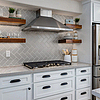White shaker kitchen in the 1410 Rockledge Rossmoor remodel featuring a herringbone tile backsplash, floating walnut shelves, stainless steel range hood, and quartz countertops in Walnut Creek.