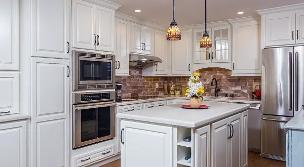 We went for a more traditional look for this kitchen remodel.  Being a downstairs unit with limited light, Light, Canvas colored cabinets help brighten the space along with a monochromatic creamy quartz countertop selection.  The rich wood tone laminate floors and faux brick look tiled backsplash bring some warmth and character into the space along with the mosaic pendants over the mini island which also features a slick Microwave drawer appliance.