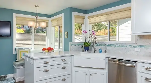 Making this kitchen functional for the specific needs of this client were what was most important in this project. The client hated the original layout and found it a hard space to work in. This new layout gave her the desired countertop/workspace between the sink and cooktop, with the refrigerator in a convenient location with landing space at the end of the peninsula. We were also able to put in a large pantry space with sliding frosted glass pocket doors and a quaint bench seat area tucked in behind the new sink peninsula. The kitchen and entry/dining room were made more open to each other and we were able to also include a bar fridge and special charging station drawer to meet other specific needs of the client. Cork flooring, Corian countertops, an apron sink, marble and glass tile backsplash are all featured in this kitchen.