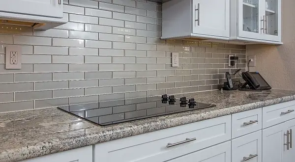 White kitchen cabinets with granite countertops, cooktop, and subway tile backsplash in Rossmoor, Walnut Creek. Terra Granada Whole House Remodel | Rossmoor, Walnut Creek