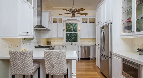 This Victorian home already had great bones with beautiful high ceilings but was dated and the kitchen was a mess. To highlight the ceiling we did a stacked molding design that extended down on the wall and out on the ceiling. Additionally stacked cabinetry featuring lighted upper glass display cabinets was part of the design adding drama and height. Other interesting lighting was featured in the space, including above and undercabinet LED tape lights, sconces in sides of the cabinets over the sink, and overhead decorative fixtures. Quartz countertops, tile backsplash and custom hardwood flooring was also installed in the space.